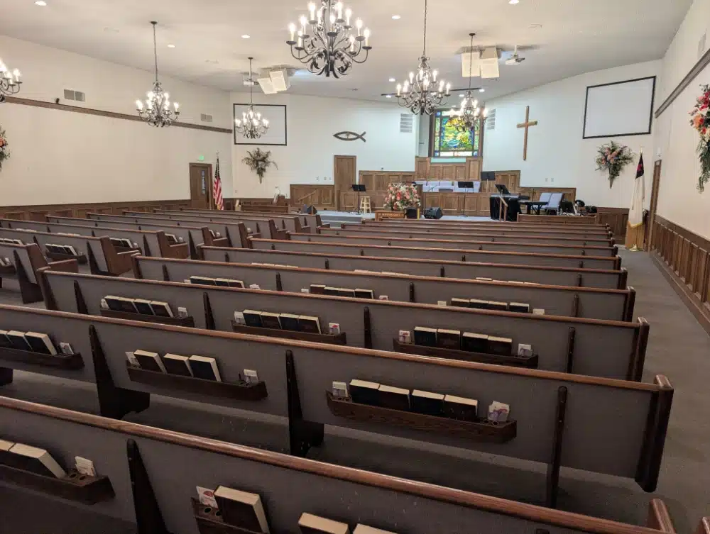 Interior of the Comfort Baptist Church sanctuary with pews, altar, stained glass window, and chandeliers